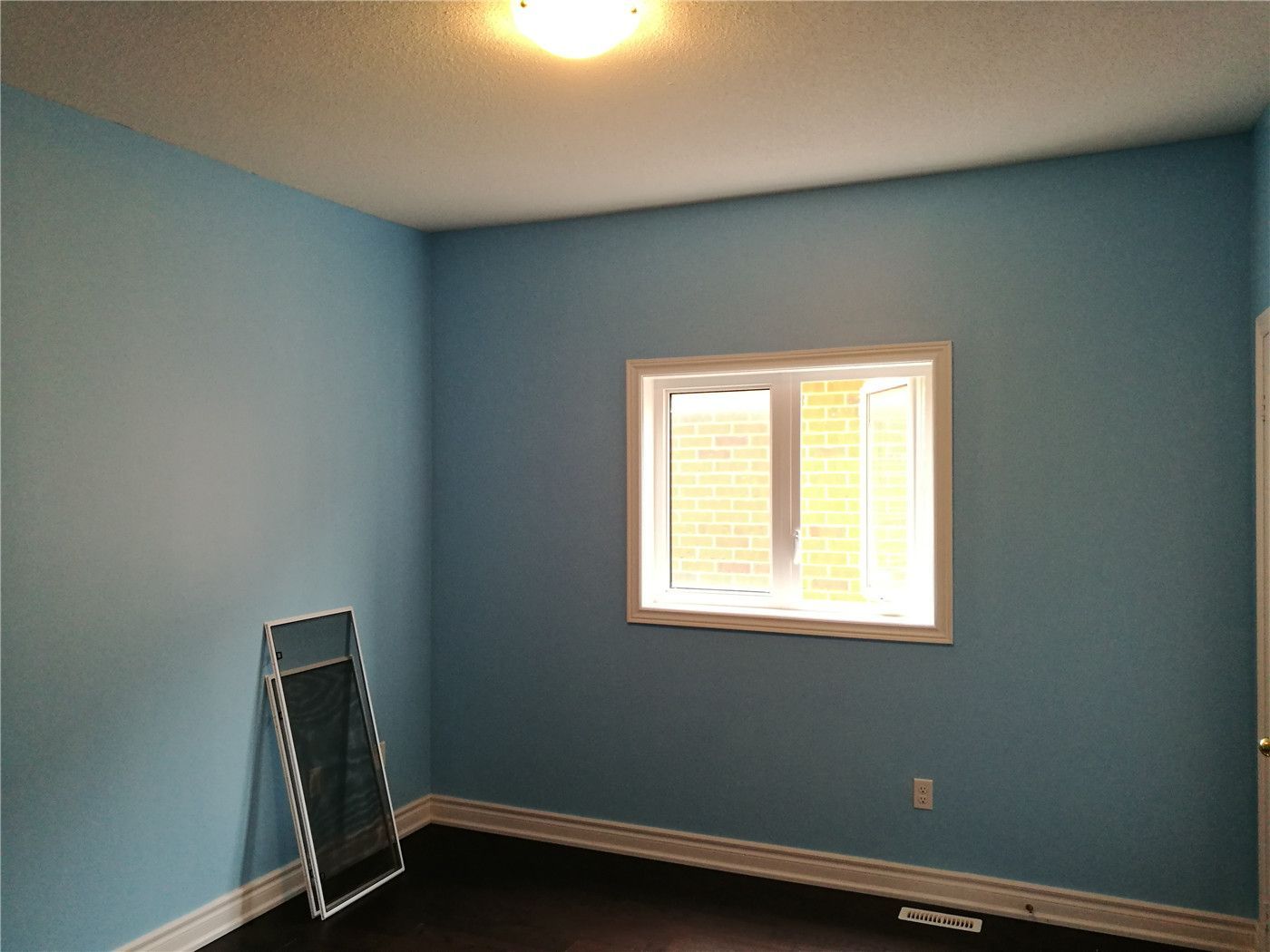 This image shows a bedroom after a Markham interior renovation, featuring fresh blue wall paint, clean trim work, updated flooring, and a window that enhances natural light and overall comfort.