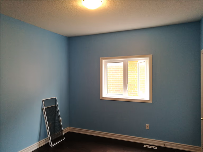 This image shows a bedroom after a Markham interior renovation, featuring fresh blue wall paint, clean trim work, updated flooring, and a window that enhances natural light and overall comfort.