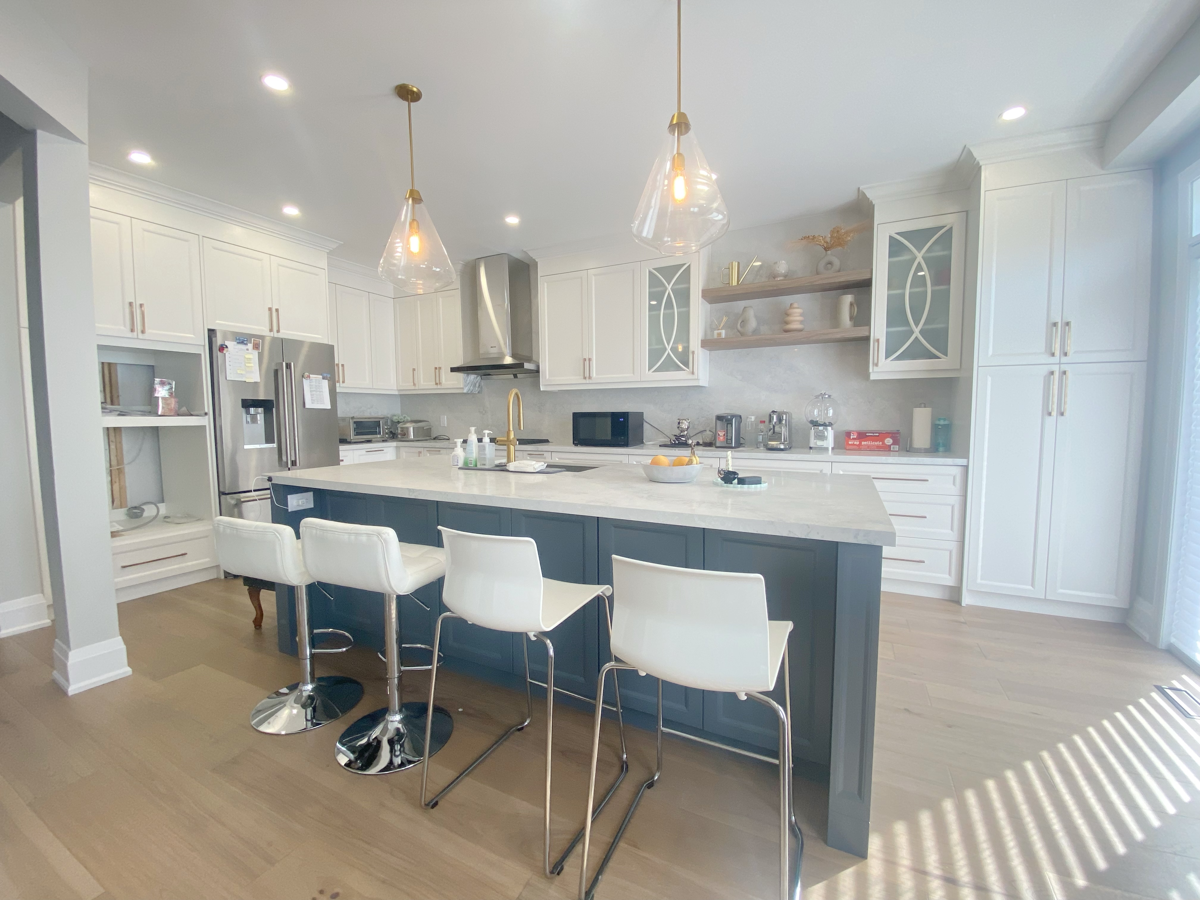 A spacious open-concept kitchen completed as part of a Richmond Hill interior renovation. This kitchen renovation features a large central island with seating, quartz countertops, custom cabinetry, modern pendant lighting, and integrated stainless steel appliances.