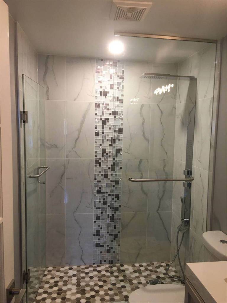 This bathroom shower renovation in Newmarket combines elegant marble-pattern wall tiles with smaller accent tiles to create a visually balanced design. The contrast between the large marble surface and the decorative small tiles adds texture and depth while defining different areas of the shower space.