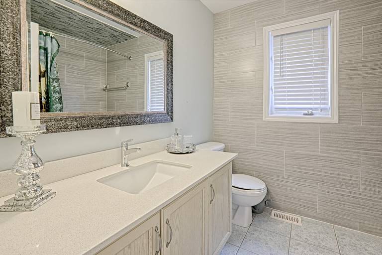 This clean bathroom vanity showcases a simple and lovely interior design with a quartz countertop, light wood cabinetry, and neutral wall tile finishes. The large framed mirror enhances brightness and visual depth, while the streamlined sink and storage provide everyday practicality. This bathroom design emphasizes cleanliness, functionality, and timeless appeal, making it suitable for family homes and long-term residential use.