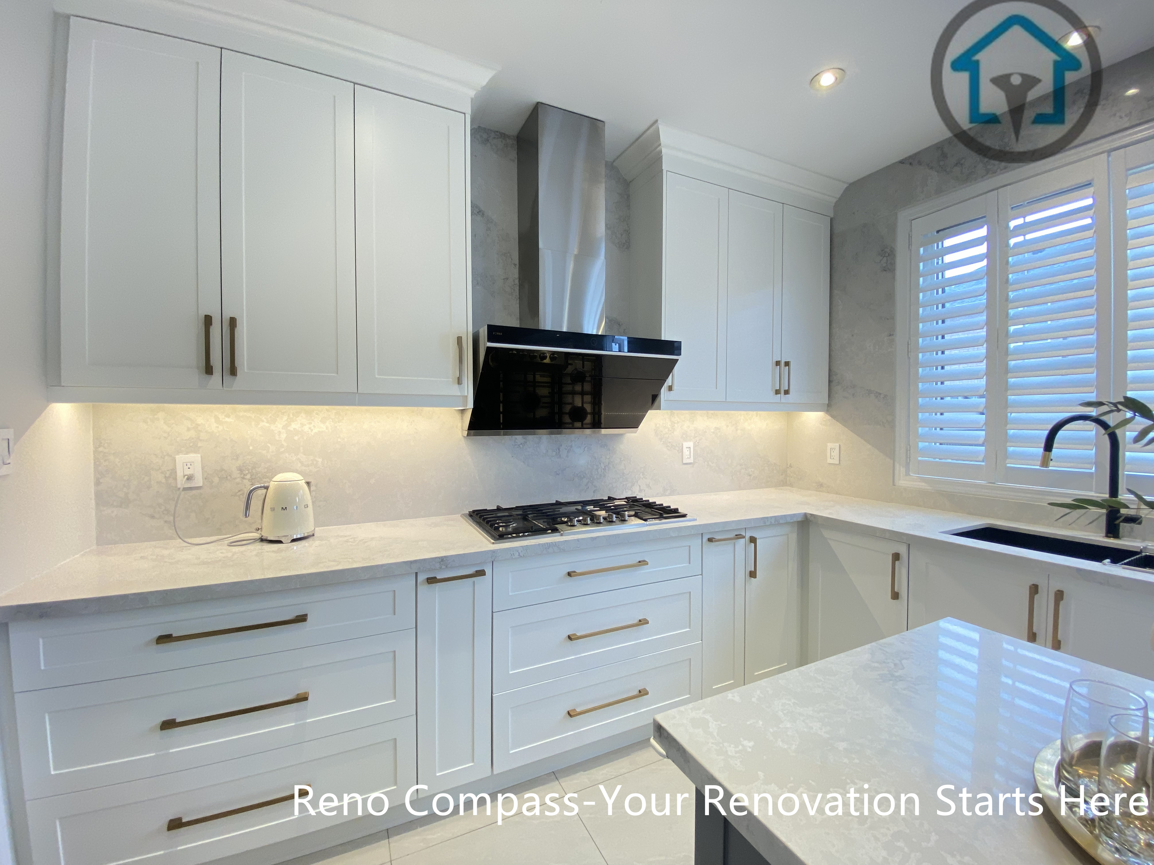 This image highlights the custom cabinetry wall of a Markham kitchen renovation, featuring full-height white cabinets, a built-in gas cooktop, and a sleek stainless steel range hood as the focal point. Under-cabinet lighting and a light stone backsplash enhance brightness while maintaining a clean, cohesive look. Designed and built by Reno Compass, this kitchen reflects a balance of refined detailing and everyday functionality for homeowners in Markham.