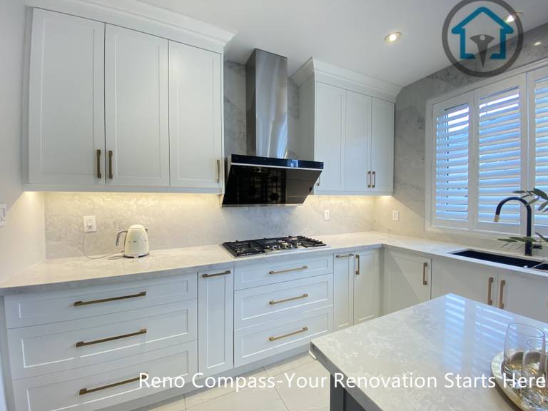 This image highlights the custom cabinetry wall of a Markham kitchen renovation, featuring full-height white cabinets, a built-in gas cooktop, and a sleek stainless steel range hood as the focal point. Under-cabinet lighting and a light stone backsplash enhance brightness while maintaining a clean, cohesive look. Designed and built by Reno Compass, this kitchen reflects a balance of refined detailing and everyday functionality for homeowners in Markham.