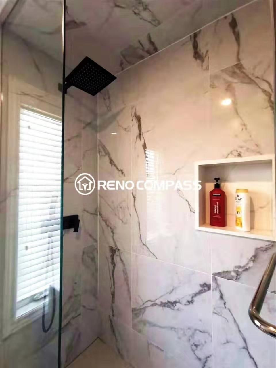 Contemporary bathroom renovation featuring a glass-enclosed shower with marble-look wall tiles, a matte black rainfall showerhead, and a built-in wall niche for convenient storage. The clean tile work and modern fixtures highlight the craftsmanship of a professional Toronto renovation company, delivering a functional, waterproof, and stylish shower space designed for everyday comfort and durability.