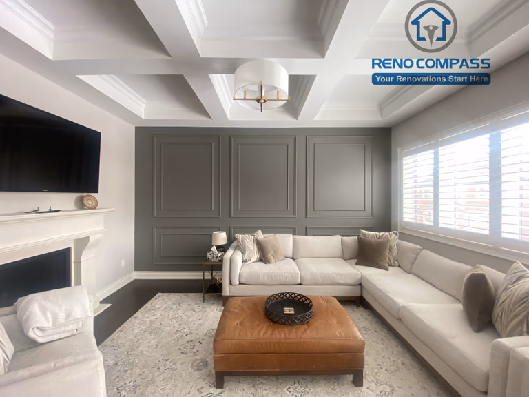 This Vaughan interior renovation features an elegant living room with a coffered ceiling, custom wall paneling, fireplace detail, and refined lighting. Neutral tones and balanced proportions create a sophisticated and comfortable space, completed by a professional Toronto renovation company.
