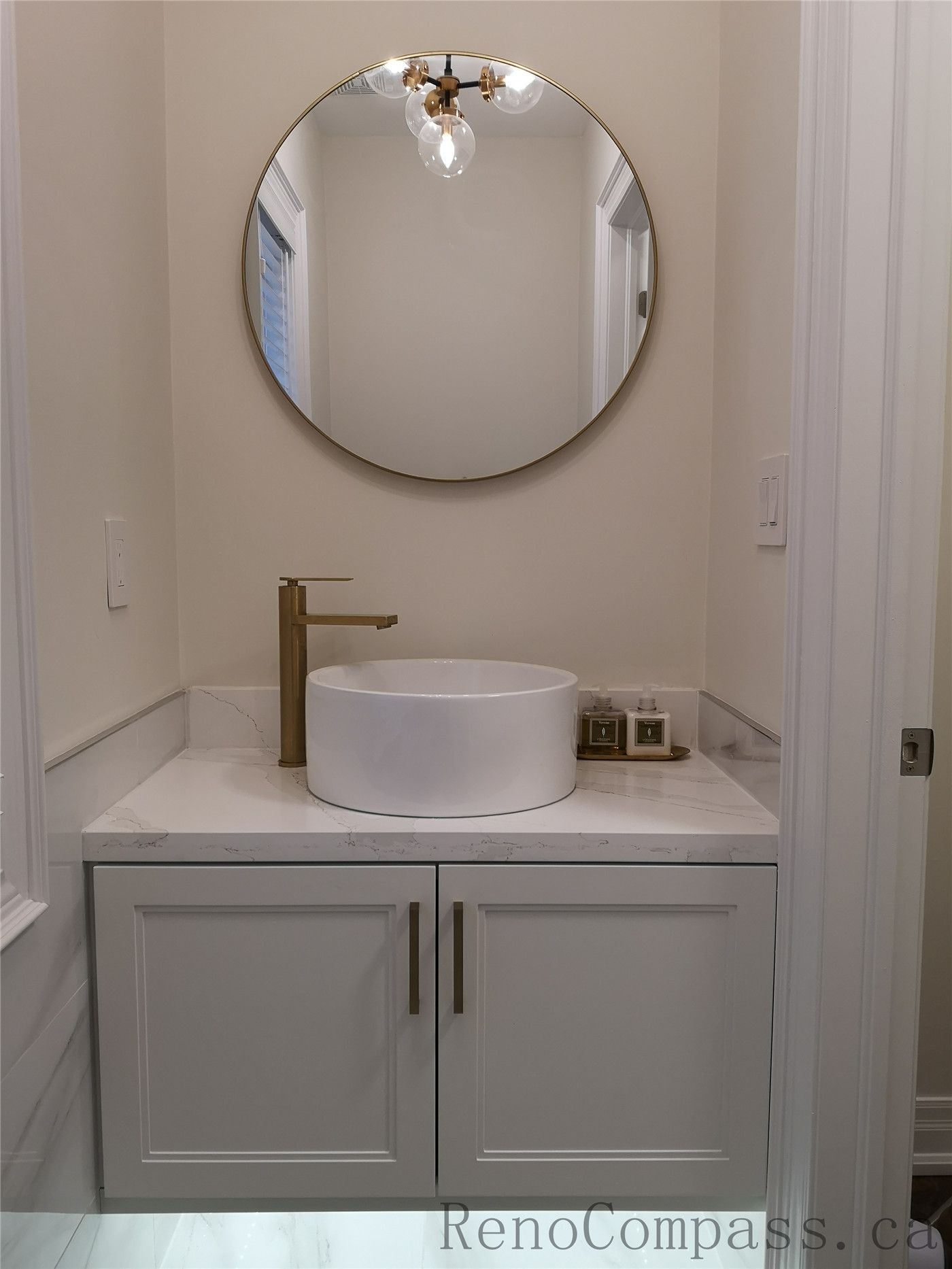 This Aurora bathroom renovation features a modern vanity with a round wall mirror, vessel sink, quartz countertop, and elegant brushed gold faucet. The clean cabinetry and soft lighting create a bright and refined space with a timeless contemporary look. Completed by a professional Toronto renovation company focused on quality finishes, functional design, and detailed craftsmanship.