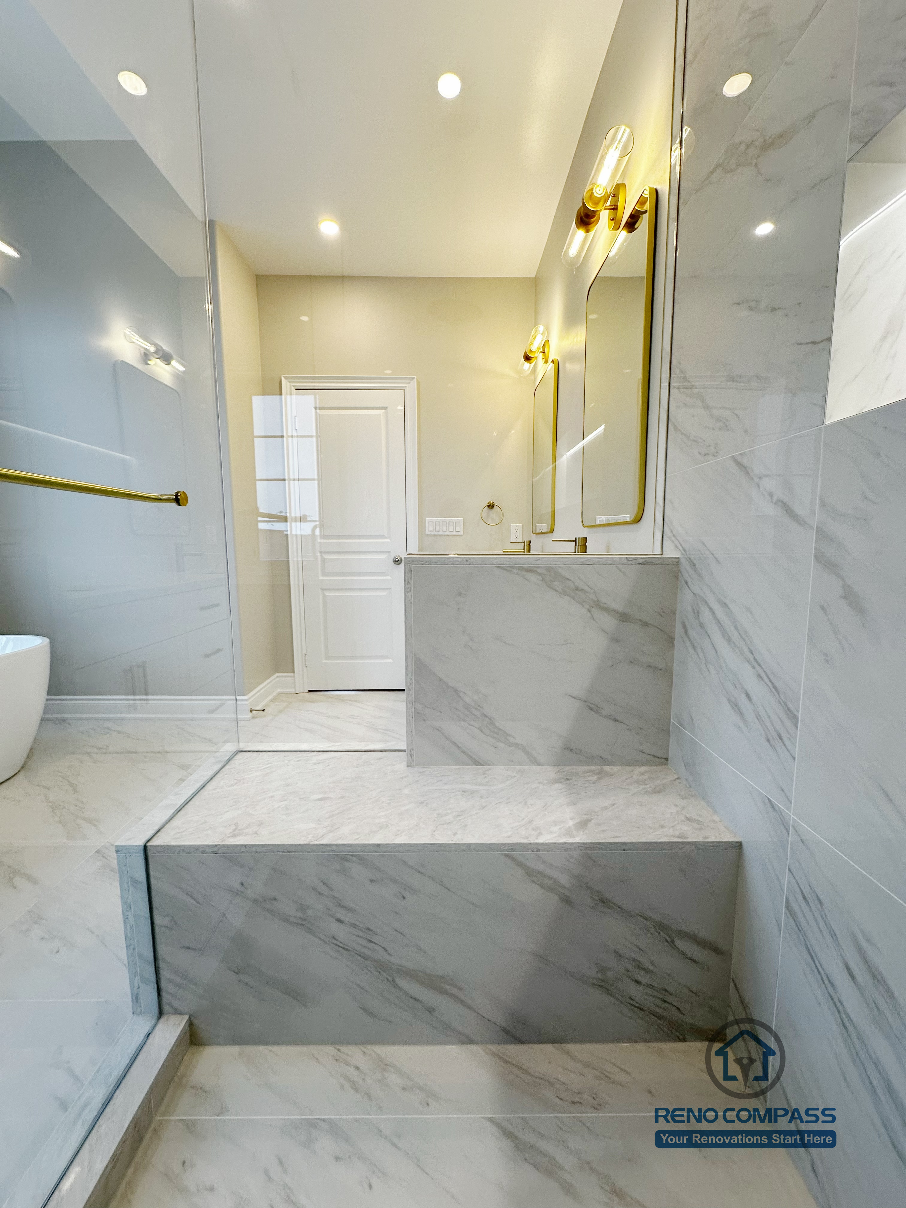 Custom raised shower platform featured in a Vaughan primary bathroom renovation, designed with marble-look porcelain tile for durability and visual continuity. The stepped layout improves water control while creating a clear transition between wet and dry zones, paired with recessed lighting and glass shower panels. Completed by a professional Toronto renovation company focused on both function and refined design.