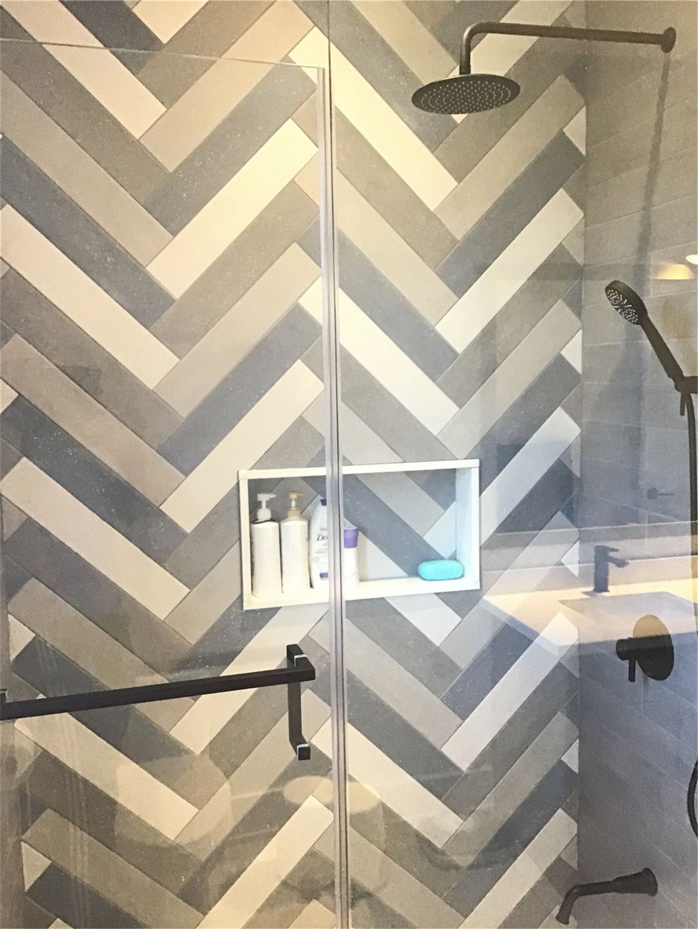 This Markham full home renovation highlights a custom shower design featuring a striking herringbone tile pattern, built-in wall niche, and sleek glass enclosure. Matte black fixtures and a modern rainfall shower system enhance both style and functionality. Completed by a trusted Toronto Renovation Company, this bathroom showcases premium materials and refined craftsmanship.