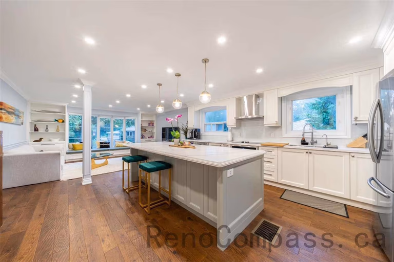 This open-concept kitchen is part of a North York interior renovation, featuring a spacious central island, custom white cabinetry, and warm hardwood flooring. Recessed ceiling lights and modern pendant fixtures enhance brightness and visual balance, while large windows provide natural daylight throughout the space. The layout improves workflow, storage, and family interaction, showcasing a practical yet elegant kitchen renovation solution commonly seen in high-quality Toronto interior renovation projects.