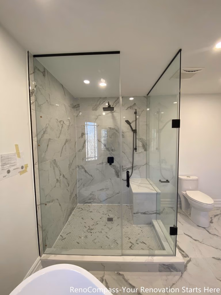 This Thornhill master bathroom renovation presents a bright, open layout featuring a double sink vanity, a freestanding bathtub, and a frameless glass walk-in shower. Marble-look porcelain tiles unify the floor and shower walls, creating a seamless and elegant visual flow throughout the space. Matte black fixtures add modern contrast, while recessed lighting and natural daylight enhance brightness and spatial balance. The thoughtful layout improves functionality, comfort, and long-term usability, delivering a refined and timeless bathroom design.