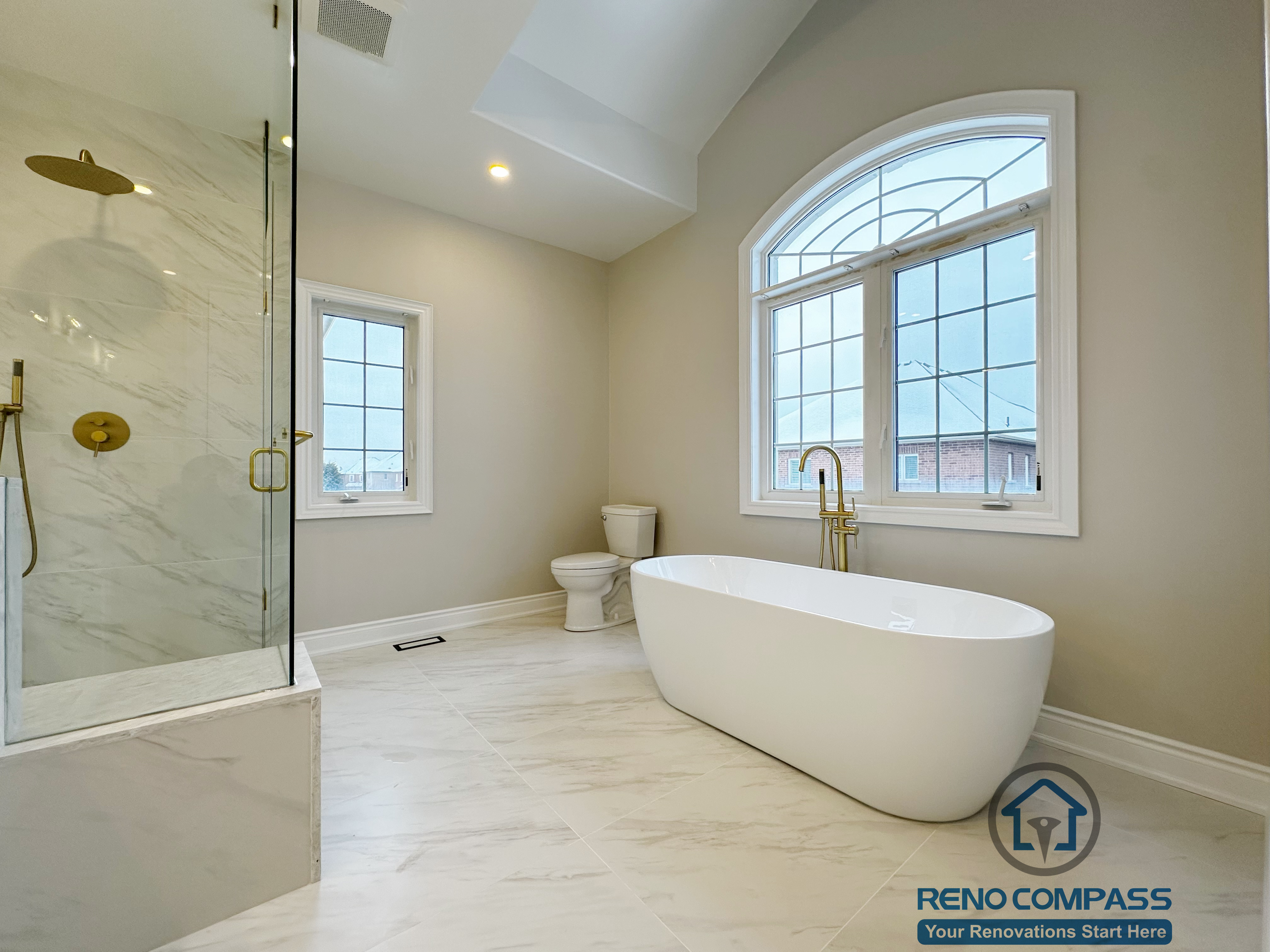 Open and airy layout in a Vaughan primary bathroom renovation, featuring a freestanding soaking tub placed near large windows for natural light, paired with a frameless glass walk-in shower and marble-look porcelain flooring. Designed to create a spa-inspired atmosphere, this project was completed by a professional Toronto renovation company focused on comfort, flow, and timeless finishes.
