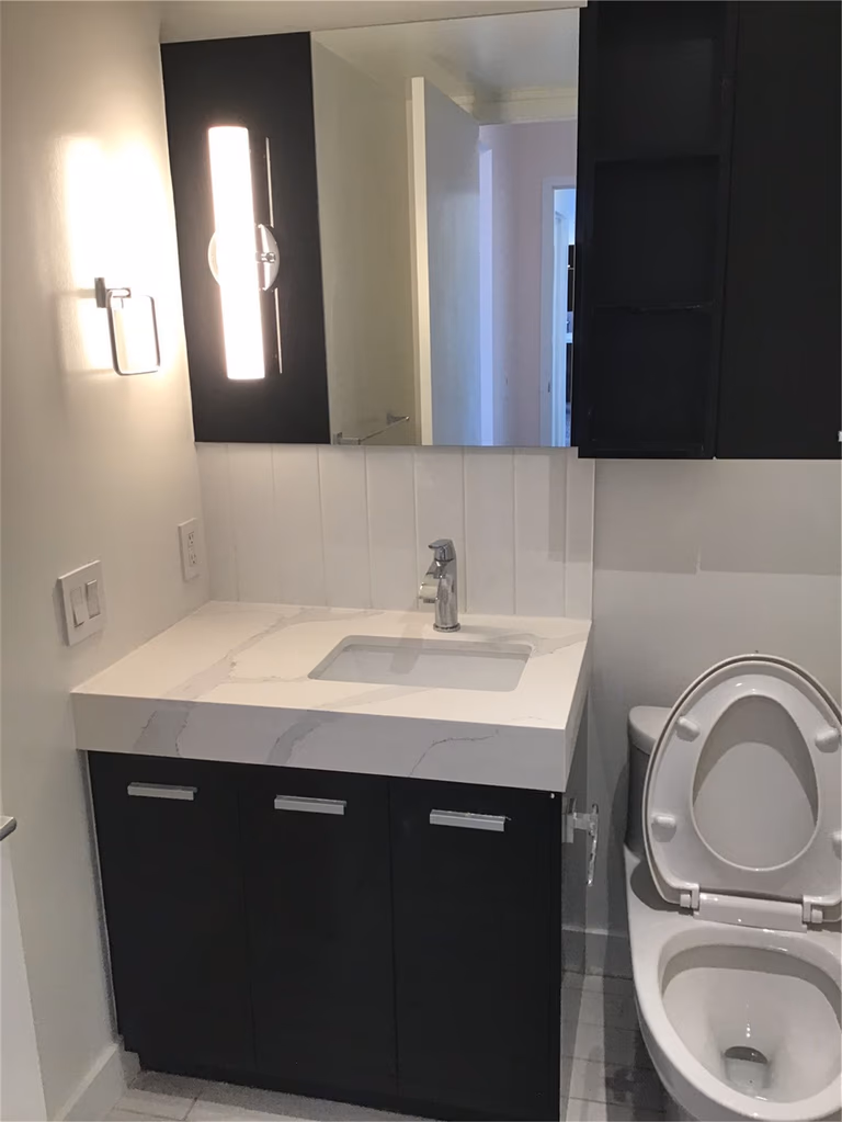 This North York condo renovation features a modern powder room with a black vanity, quartz countertop, integrated sink, and wall-mounted lighting. The compact layout maximizes functionality while maintaining a clean, contemporary look ideal for urban condo living.