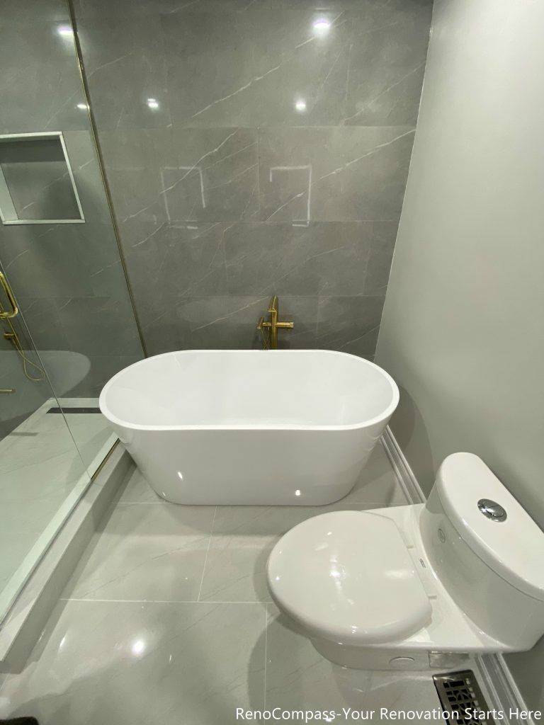 This Oakville master bathroom renovation features a sleek freestanding bathtub paired with premium gold floor-mounted fixtures and large-format marble-look wall tiles. The clean layout integrates a glass-enclosed shower and modern toilet placement, creating a functional yet luxurious spa-style bathroom environment. Completed by a professional Toronto renovation company, this upgrade enhances comfort, improves space efficiency, and delivers a timeless modern design that increases both daily living quality and overall property value.