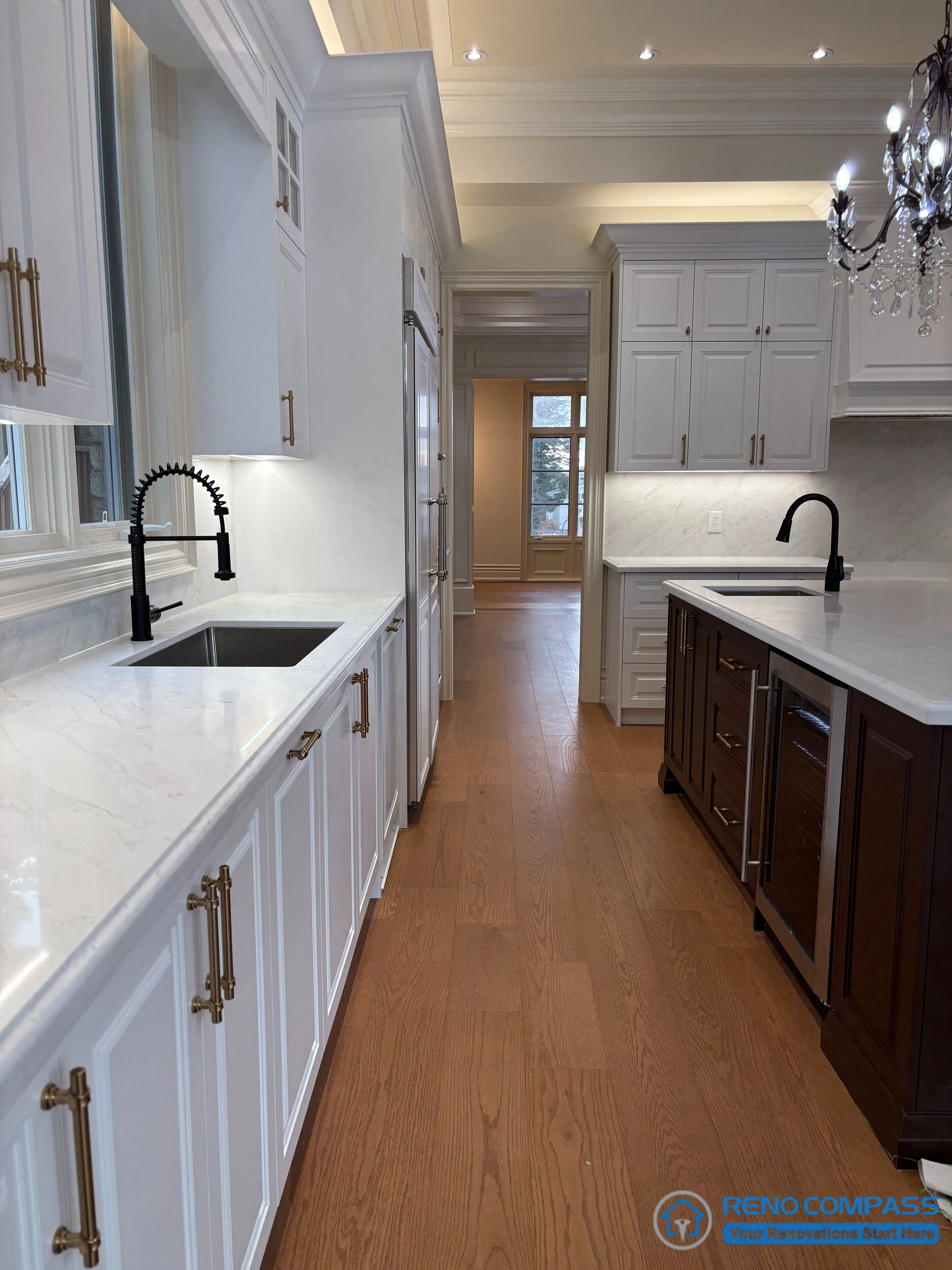 This image captures the primary work area of a European-style kitchen, featuring continuous full-height cabinetry, quartz countertops, and an integrated sink run along the perimeter wall. The linear arrangement supports efficient daily use while maintaining visual order and consistency. Traditional paneled doors, classic hardware, and concealed lighting reinforce the kitchen’s architectural character. The relationship between the perimeter workspace and the central island is clearly defined, allowing functional separation without disrupting overall composition. This view highlights practical kitchen planning and refined craftsmanship within a high-end Richmond Hill interior renovation.