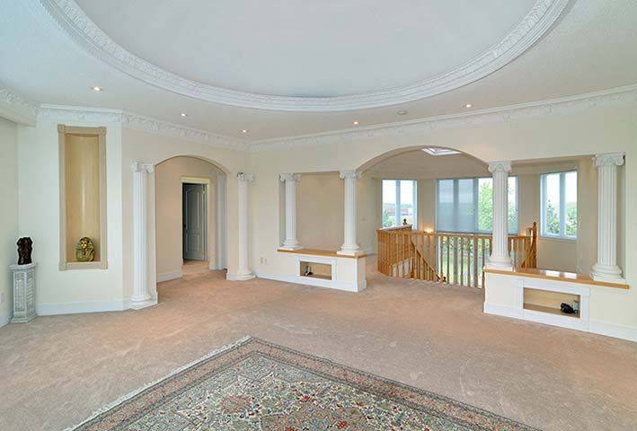 Elegant upper family room from a luxury Toronto home renovation featuring decorative architectural columns, curved ceiling design, and an open-concept layout overlooking the staircase below. Large windows bring natural light into the space, creating a bright and comfortable gathering area for family living. This custom interior renovation project was completed by Reno Compass, a trusted Toronto Renovation Company specializing in luxury home rebuilds and interior renovations across the Greater Toronto Area.
