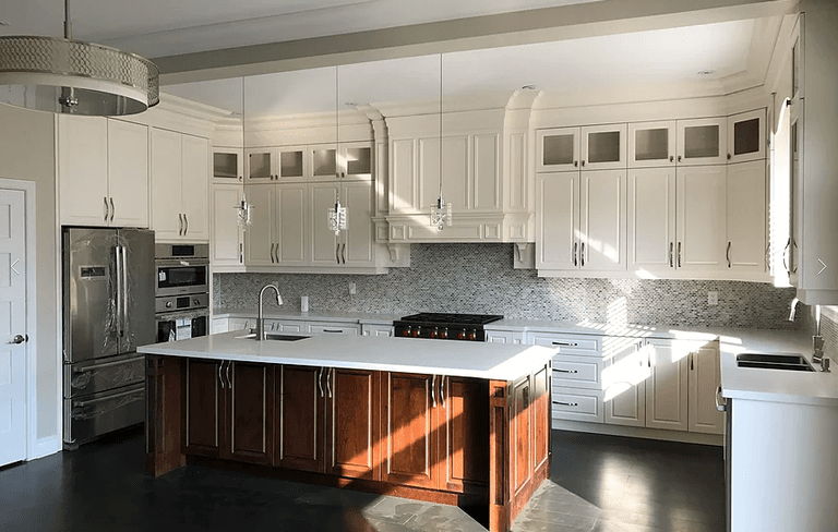 This modern Markham kitchen renovation features custom white cabinetry, a large central island with dark wood base, quartz countertops, and built-in stainless steel appliances. Elegant mosaic backsplash, detailed crown molding, and pendant lighting create a bright and luxurious cooking space. Completed by a professional Toronto renovation company, this kitchen combines functionality, storage, and timeless design for modern family living.