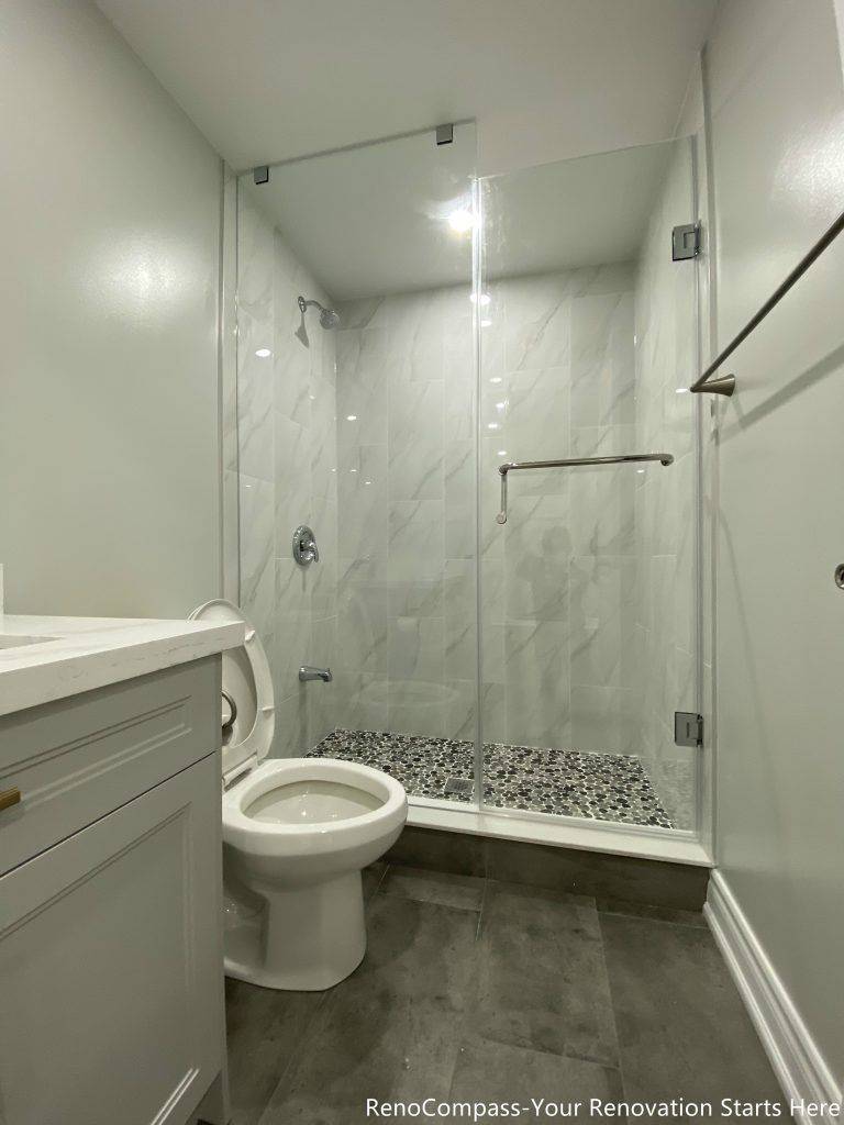 This Oakville basement bathroom renovation features a modern walk-in glass shower with marble-style wall tiles, pebble shower flooring, and sleek chrome fixtures for a clean and contemporary finish. The space is designed for both comfort and durability, combining water-resistant materials with efficient layout planning to maximize functionality in a compact basement setting. Completed by a trusted Toronto renovation company, this bathroom upgrade enhances daily living while adding long-term value and modern appeal to the home.