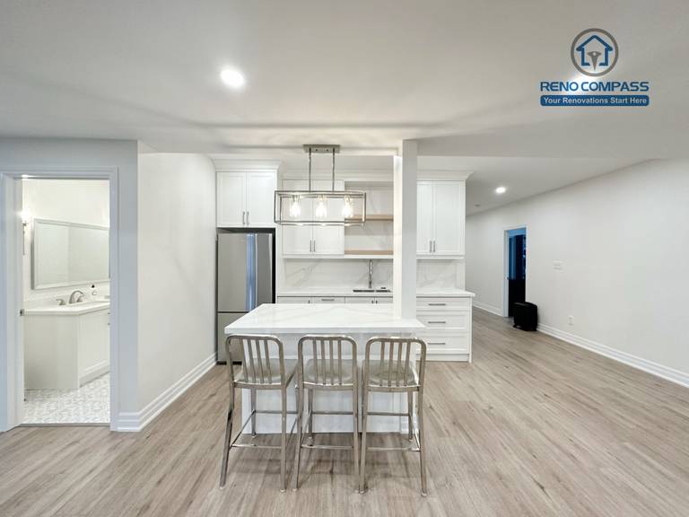 This Bradford basement renovation transforms the lower level into a bright, open-concept living and entertainment space. The layout integrates a custom wet bar with full-height cabinetry, quartz countertop, and built-in sink, creating a functional transition between the entertainment zone and seating area. Recessed LED lighting throughout the ceiling enhances brightness and eliminates the typical basement dark feel, while durable wood-look flooring provides warmth and continuity across the space. Structural columns were carefully incorporated into the design to maintain openness without compromising support. This basement renovation reflects Reno Compass’ approach to practical space planning, clean finishes, and long-term usability for modern family living.