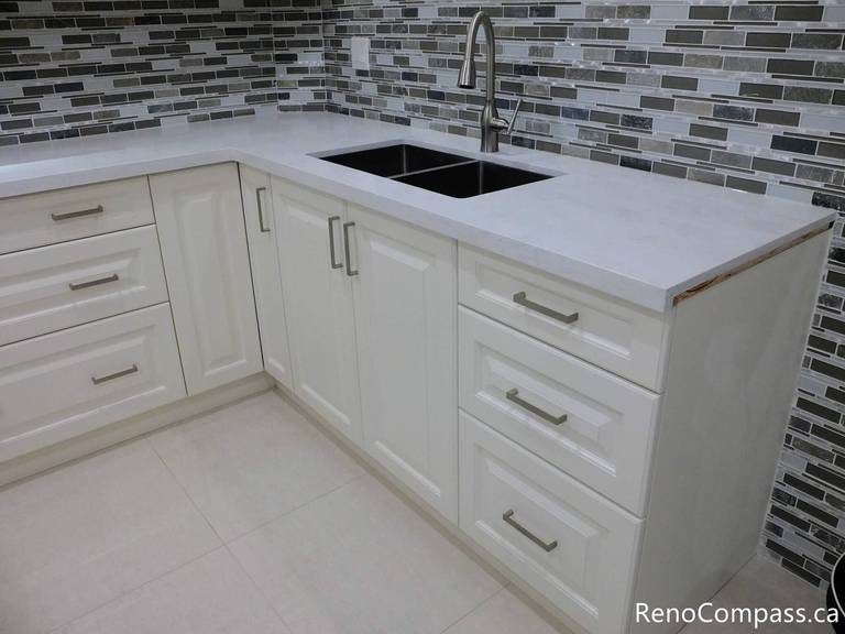 Detailed view of a Markham basement kitchen renovation showcasing white shaker cabinets, quartz countertop, double undermount sink, and a modern mosaic tile backsplash. The clean lines and practical layout enhance both durability and style in this finished basement space. Completed by a professional Toronto renovation company, this project reflects precision craftsmanship and thoughtful kitchen design.