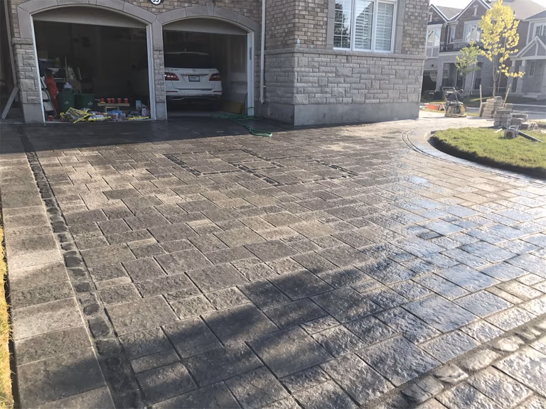 Front yard landscaping renovation in Toronto featuring a curved interlocking driveway with decorative stone borders. The design enhances curb appeal while creating a durable and visually appealing driveway layout that complements the home’s architecture.