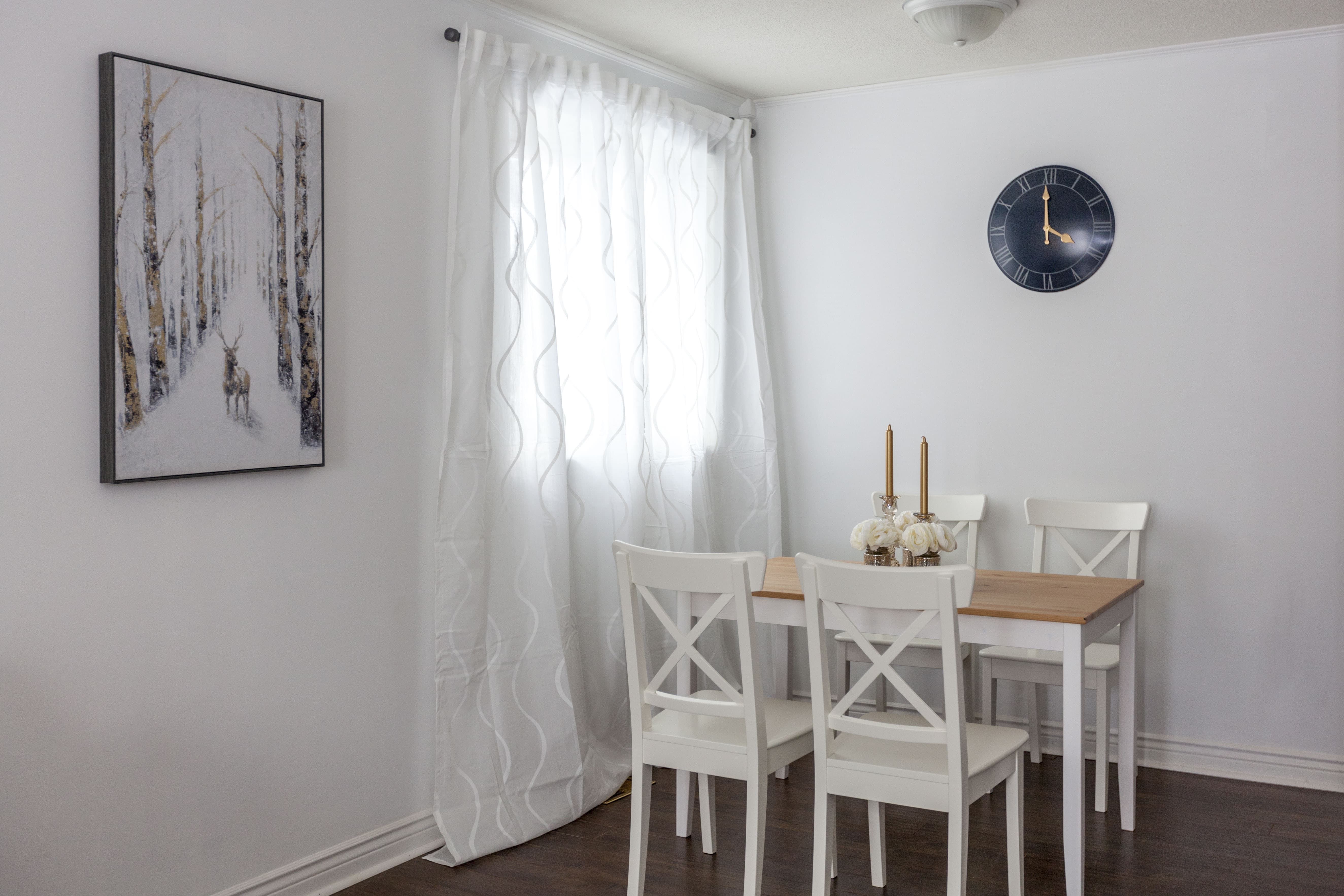 This Toronto interior renovation features a bright and welcoming dining area with a wooden table set and white chairs. Natural light flows through the large window with soft curtains, enhancing the clean and modern atmosphere. The space is designed for everyday dining and small gatherings, showcasing the balance of functionality and comfort delivered by a professional Toronto Renovation Company.