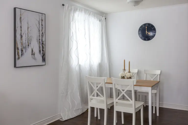 This Toronto interior renovation features a bright and welcoming dining area with a wooden table set and white chairs. Natural light flows through the large window with soft curtains, enhancing the clean and modern atmosphere. The space is designed for everyday dining and small gatherings, showcasing the balance of functionality and comfort delivered by a professional Toronto Renovation Company.