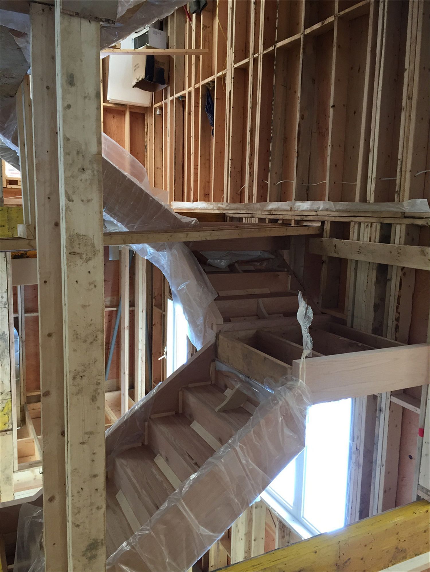 This image shows a multi-level staircase installation during a residential renovation project in Toronto. The custom wood staircase structure is carefully positioned within the framed interior, connecting different floors while ensuring proper support and alignment. Protective wrapping helps preserve the stair components during construction. As a trusted Toronto Renovation Company, Reno Compass Inc. specializes in custom staircase installation and structural renovation, delivering durable and well-crafted stair systems for homes across Toronto and the Greater Toronto Area.
