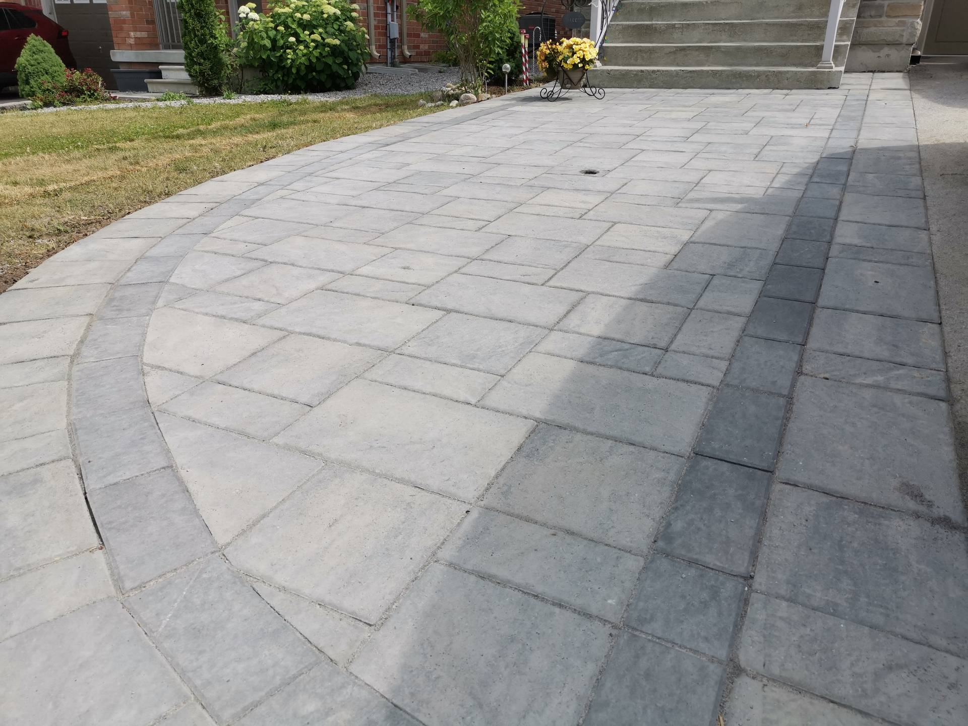 This Aurora interlocking driveway features a curved border detail that adds visual flow and refined craftsmanship to the overall layout. Large-format concrete pavers are precisely installed to create a smooth, durable surface while the contrasting curved inlay defines the driveway edge and enhances architectural balance. The clean alignment supports proper drainage, long-term stability, and low maintenance. This professionally completed interlocking driveway detail improves curb appeal and functionality for residential properties in Aurora.