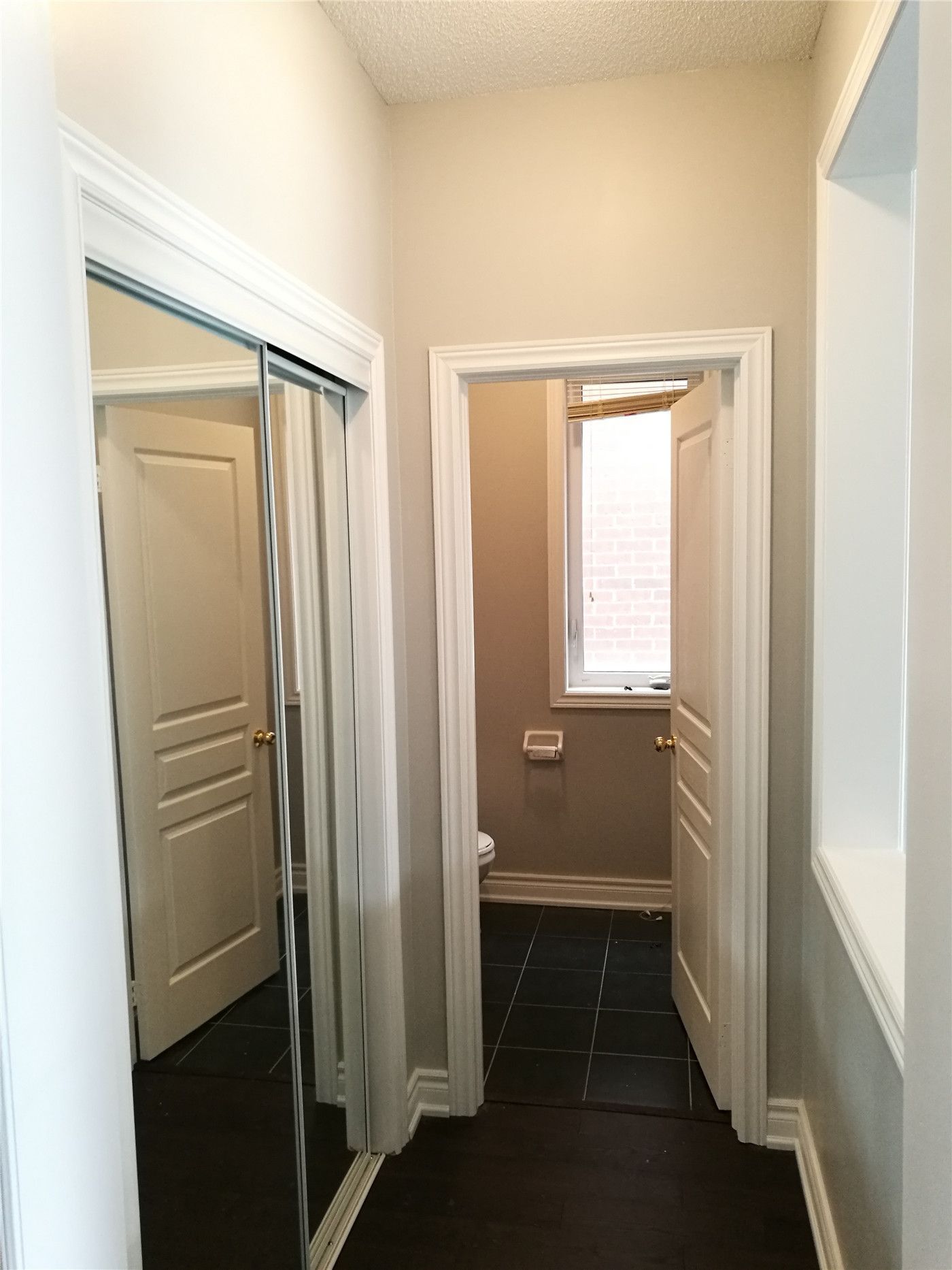 This image showcases a hallway and bathroom entrance after a Markham interior renovation, featuring clean wall finishes, upgraded doors, mirrored closet storage, and dark tile flooring that improves daily circulation and space efficiency.