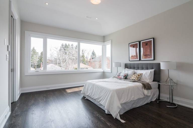 This elegant bedroom is part of a 4,500 sq ft modern home renovation in Toronto, designed to maximize natural light and comfort. Expansive corner windows brighten the space while dark hardwood flooring and soft neutral tones create a calm and contemporary atmosphere. The refined layout enhances both functionality and visual openness, reflecting the quality craftsmanship of a professional Toronto Renovation Company, Reno Compass Inc. This project highlights modern residential design tailored for luxury living.
