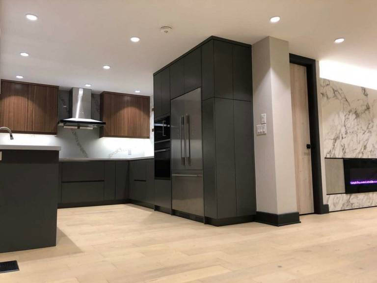 Contemporary kitchen renovation in Markham featuring custom two-tone cabinetry, built-in appliances, sleek range hood, and open-concept layout. The design integrates warm wood finishes, matte black cabinets, and modern lighting to create a functional and stylish cooking space that connects seamlessly with the living area for modern family living.
