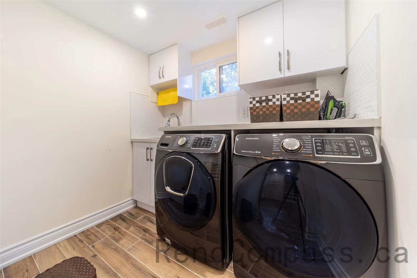 This North York interior renovation includes a clean and functional laundry room upgrade featuring modern front-load washer and dryer units, custom white cabinetry, and durable wood-look tile flooring. The design maximizes storage and efficiency with built-in cabinets, a utility sink, and bright recessed lighting. Completed by a trusted Toronto renovation company, this laundry space combines practicality and modern design to create a tidy and efficient household workspace.