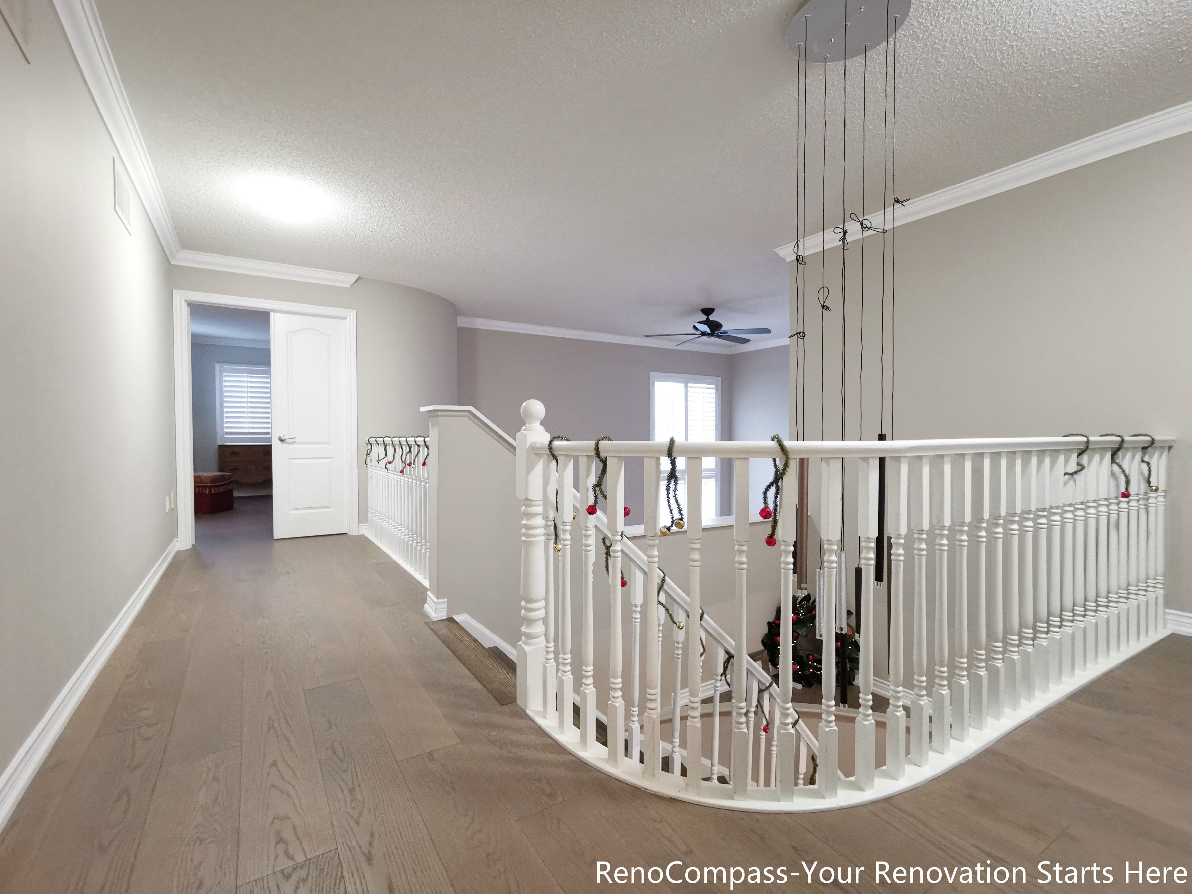 his image showcases an open hallway and staircase area completed as part of an Oakville interior renovation. Light-toned hardwood flooring extends seamlessly through the upper level, enhancing visual continuity and brightness. The curved staircase with white balusters adds architectural softness while maintaining a clean, timeless look. Neutral wall tones, crown molding, and open sightlines create a calm transition between private rooms and shared living spaces, resulting in a layout that feels both spacious and well-balanced.